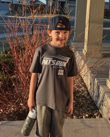 A 6-year-old boy wearing a Pat's Run T-shirt poses for a photo outside his house