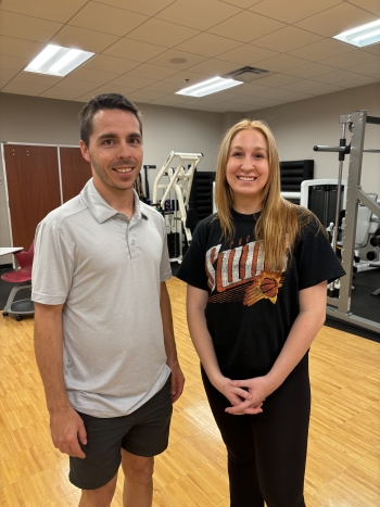 Student and professor pose for a photo in a gym.