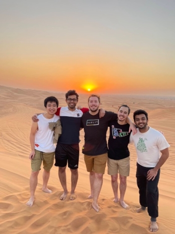 Group of five students posing on a sand dune in front of a sunset in Dubai