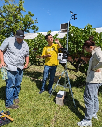 Three people set up a tool to measure flood irrigation on a lawn.