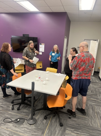 A group of people stand around a table with some objects on it