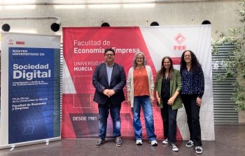 Four people pose for a photo in front of university signage in Spanish