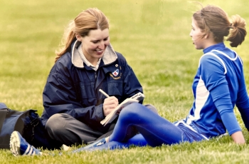 A woman interviews a soccer play as they both sit on a field