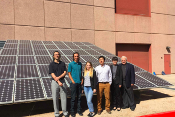 A professor and students stand in front of a solar array outside a building.