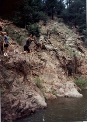 Photo of a man jumping off a small cliff into a stream