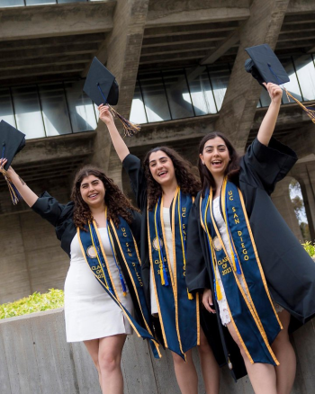 Triplets in white dresses with blue caps and gowns celebrating after college graduation