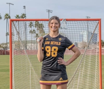 young woman with lacrosse stick in front of a lacrosse goal