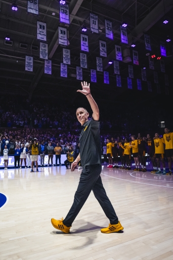 Coach walking onto basketball court waving at fans in stands