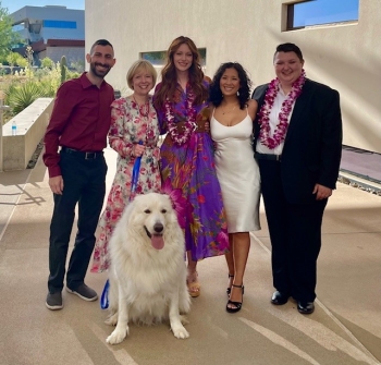 Five people, one in graduation gown, and a dog pose for a group photo