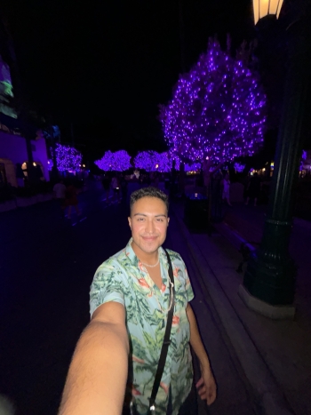 Chazz Duran, taking a selfie at night with light-wrapped trees in the background