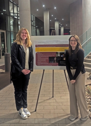 Two women stand next to a research poster.