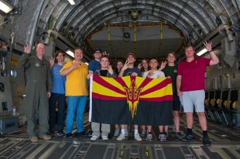 A group of students gather around inside a plane, holding up a Sun Devil pitchfork flag