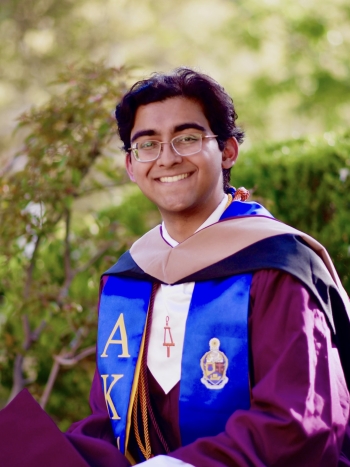 Young man with short dark hair and glasses in graduation garb