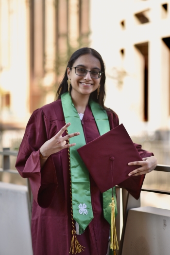 Young woman with long dark hair and glasses in graduation garb