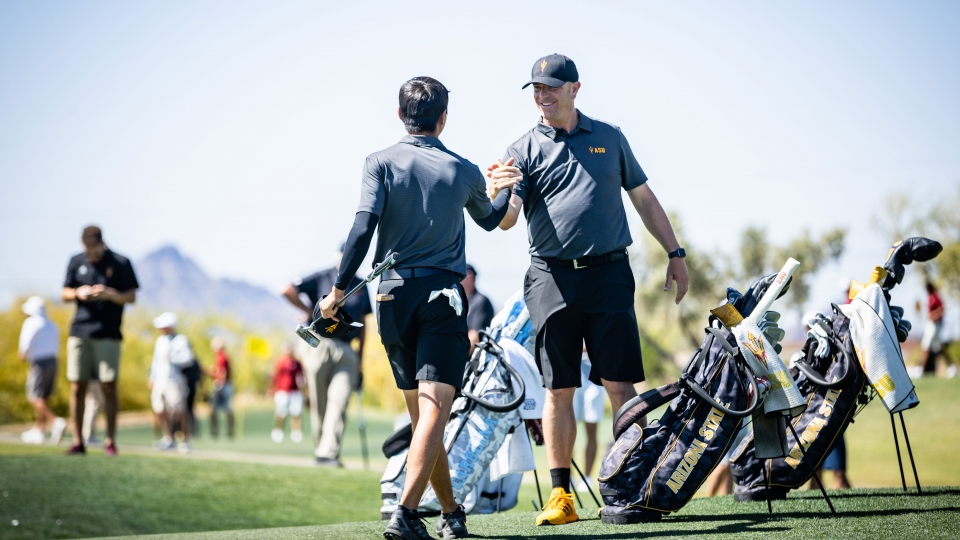 A golf coach smiles and clasps hands with a student-athlete on a golf course
