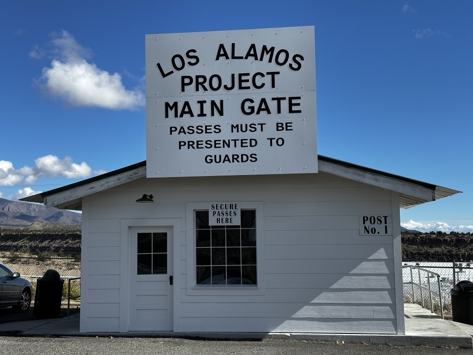 Small house-like structure with a sign that reads "Los Alamos Project Main Gate - passes must be presented to guards."