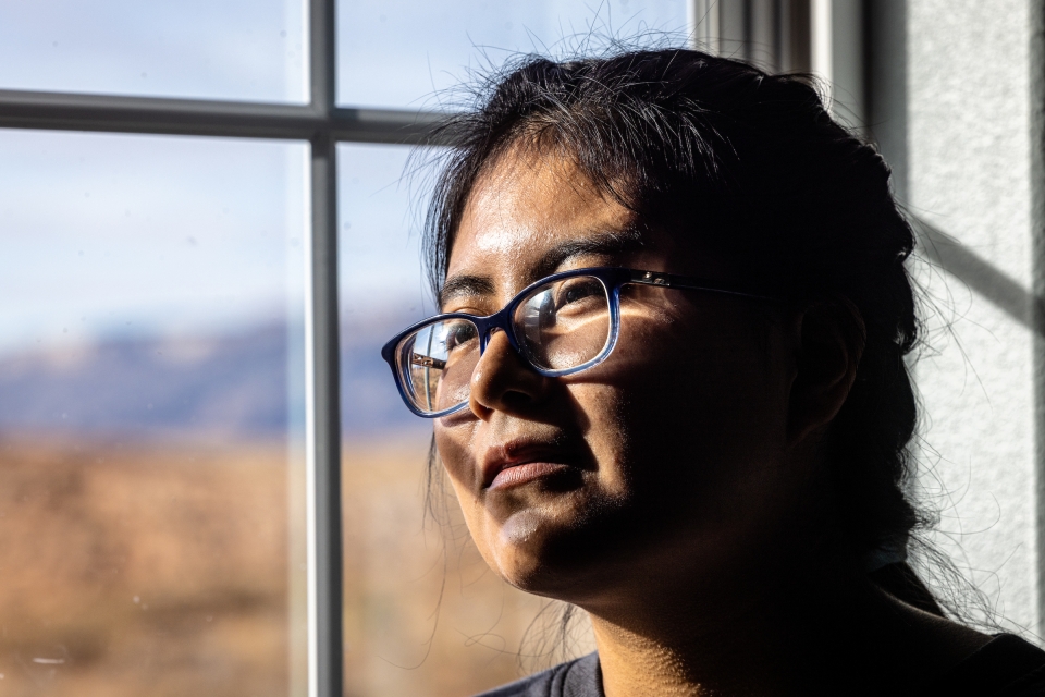 A young Native American woman looks out a window with the light playing across her face