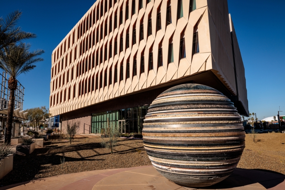 An exterior photo of the ISTB7 building with a large round, stone sculpture in front of it