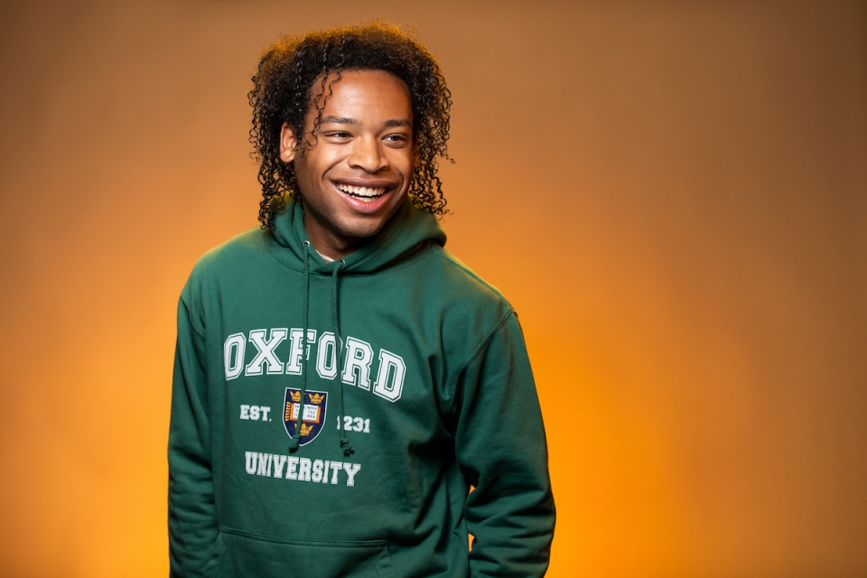Portrait of Black male student in studio, smiling, wearing an Oxford sweatshirt