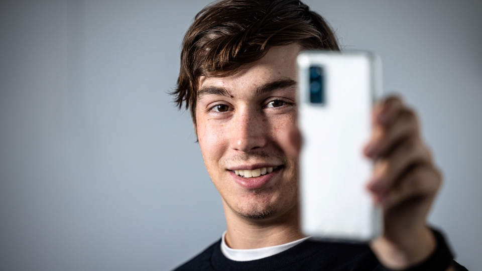 A man smiles while holding a phone up toward the camera