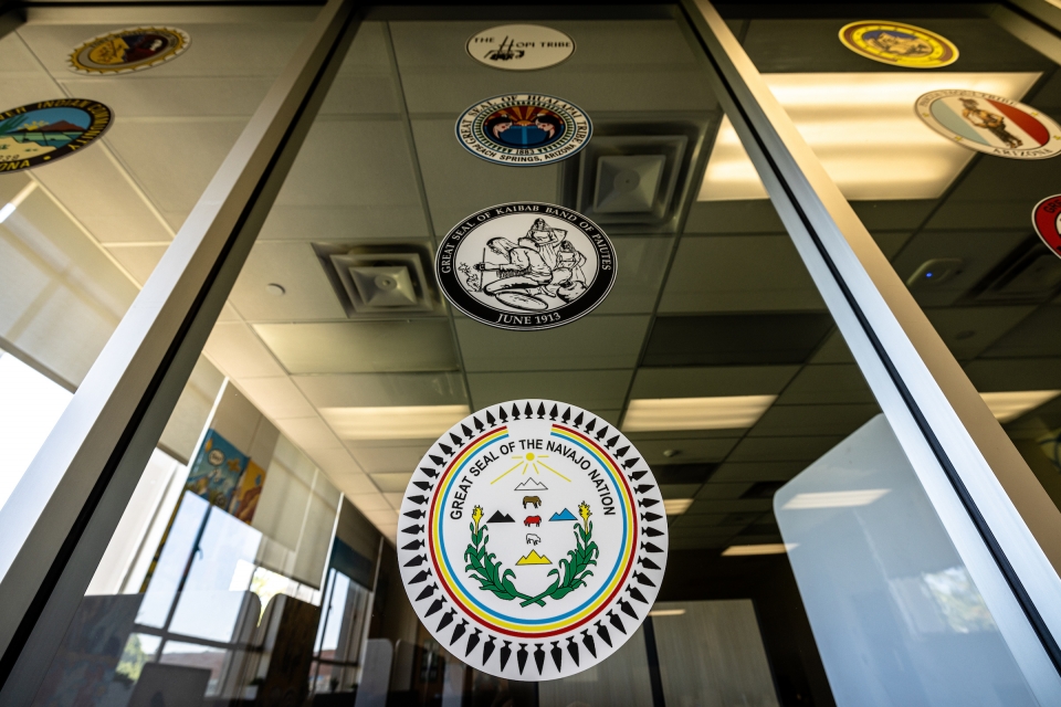 Seals of various Native nations are on a window in an office and study space