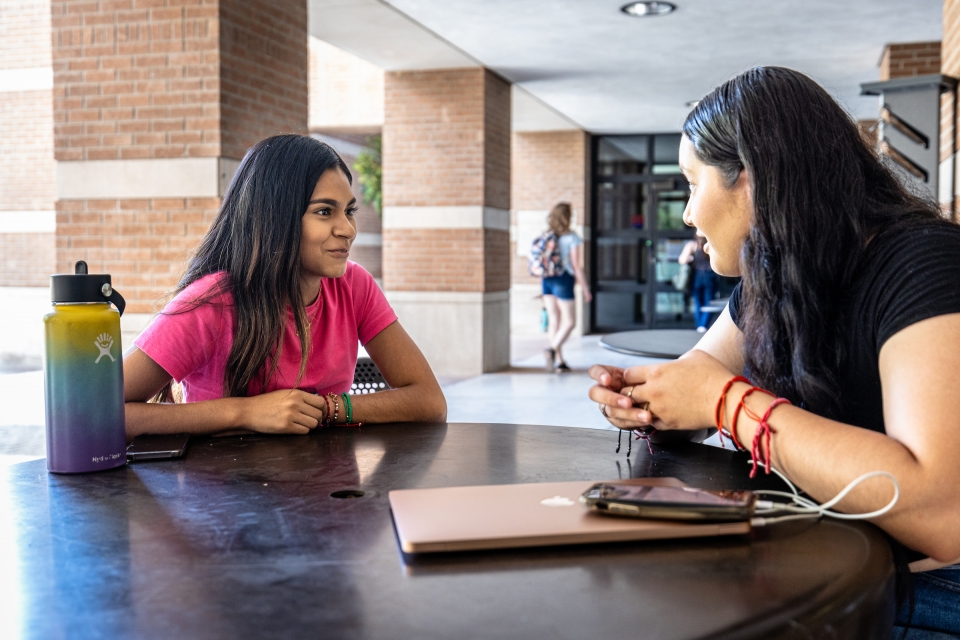 two students talking at a table outside