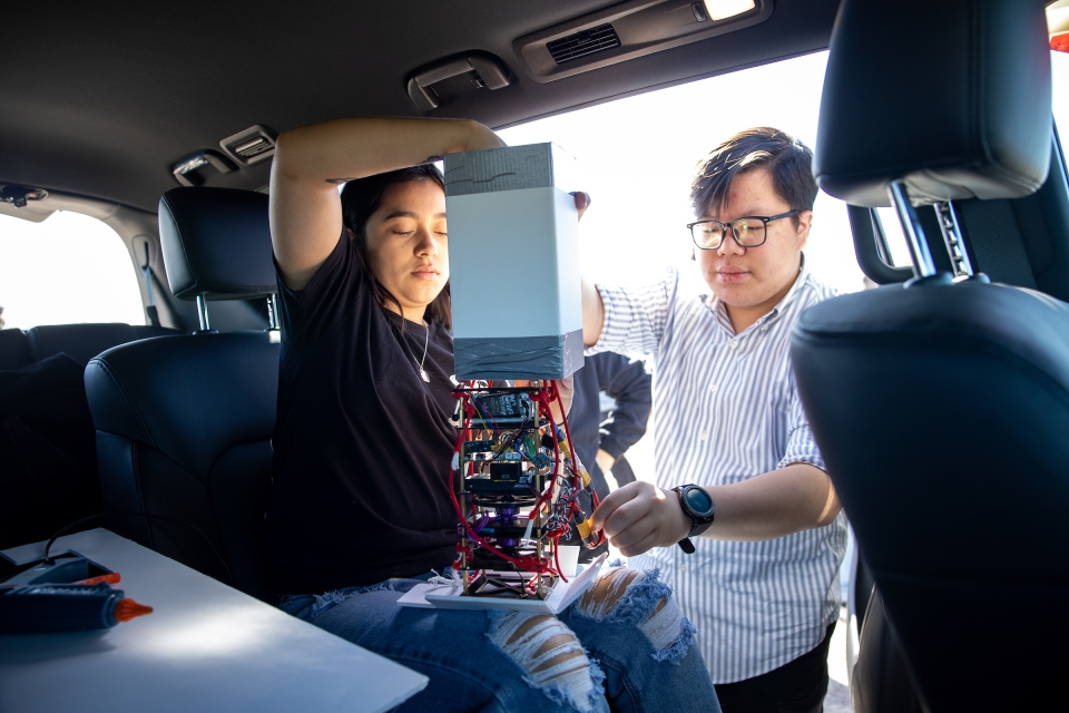 Two students prepping a payload in a car for a high-altitude weather balloon 