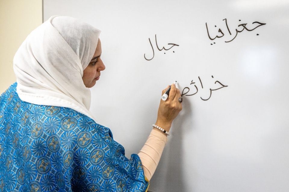 Woman writing on white board in Arabic