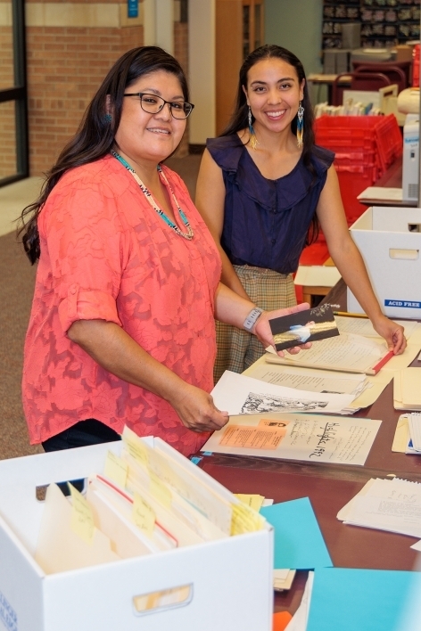 Two women handling archival materials in a library smile at the camera.