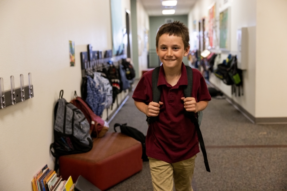 Young boy walkin through school hall wearing backpack