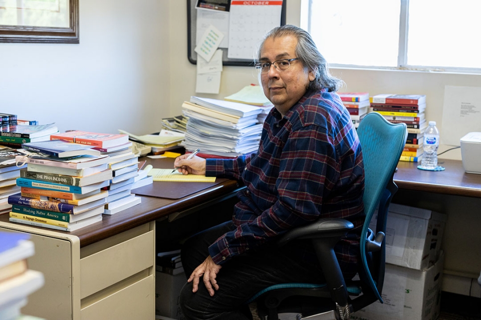 David Martinez sits in his office, surrounded by stacks of books. 
