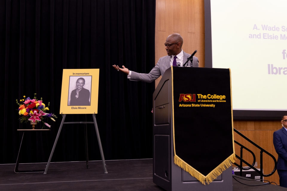 Black man behind lectern gesturing to portrait of Black woman to honor her memory