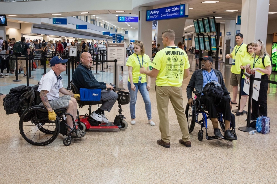 A few men in wheelchairs speak with volunteers dressed in bright yellow shirts.