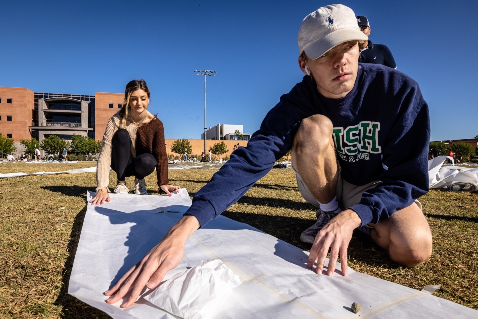 ASU students arrange large sheets of butcher paper on a grassy field.