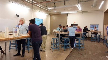 People standing at tables and talking in a large, co-working space.