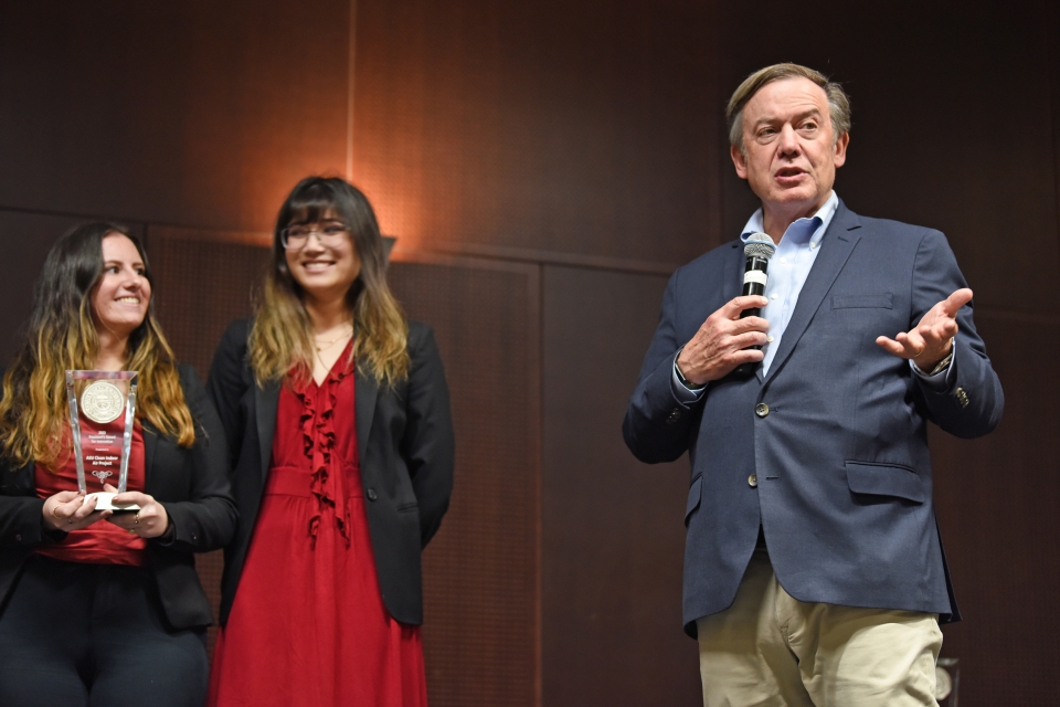 ASU President Michael Crow speaks at event while two people stand with award behind him