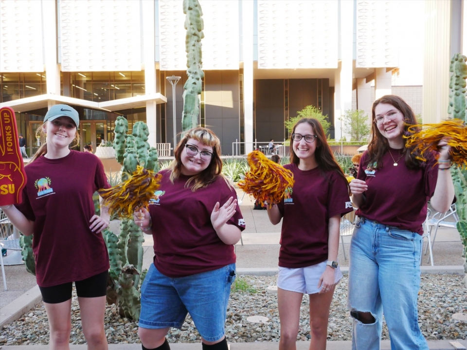ASU students wearing maroon shirts and holding gold pom poms and smiling.