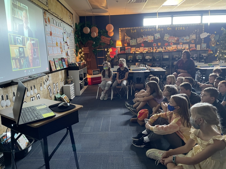 Children in a classroom watching a screen while Jane Goodall speaks.