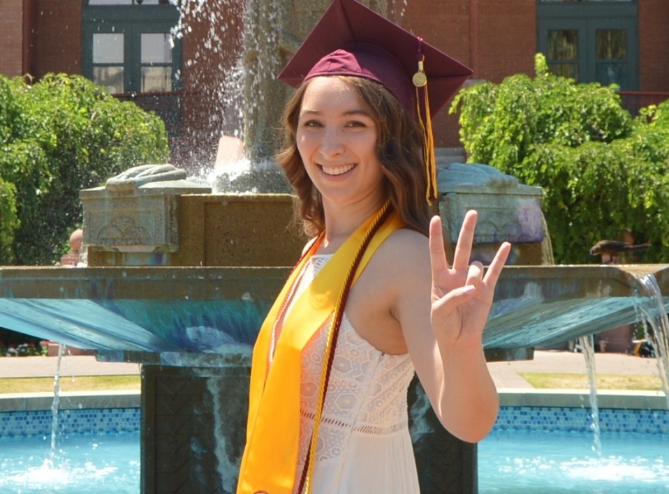 Kyra Allen in ASU graduation garb shows off a pitchfork at Old Main