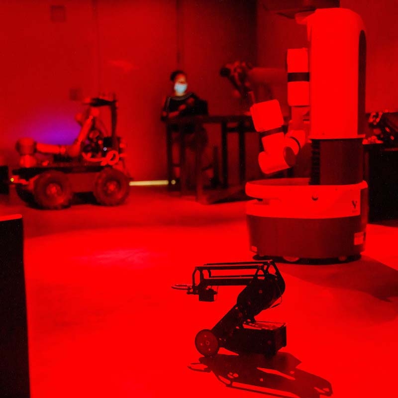 An ASU researcher experiments with two robots in an ASU lab with red lighting like the surface of Mars.