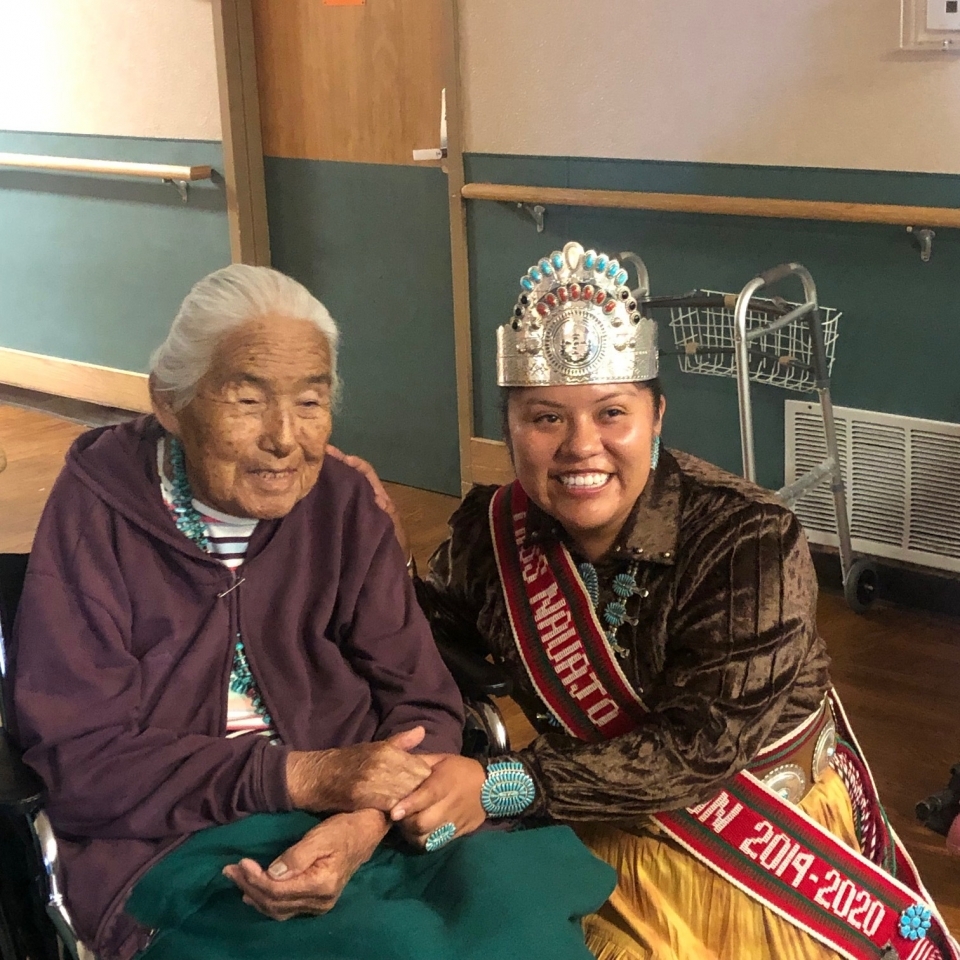 smiling woman kneeling next to smiling, seated elderly woman