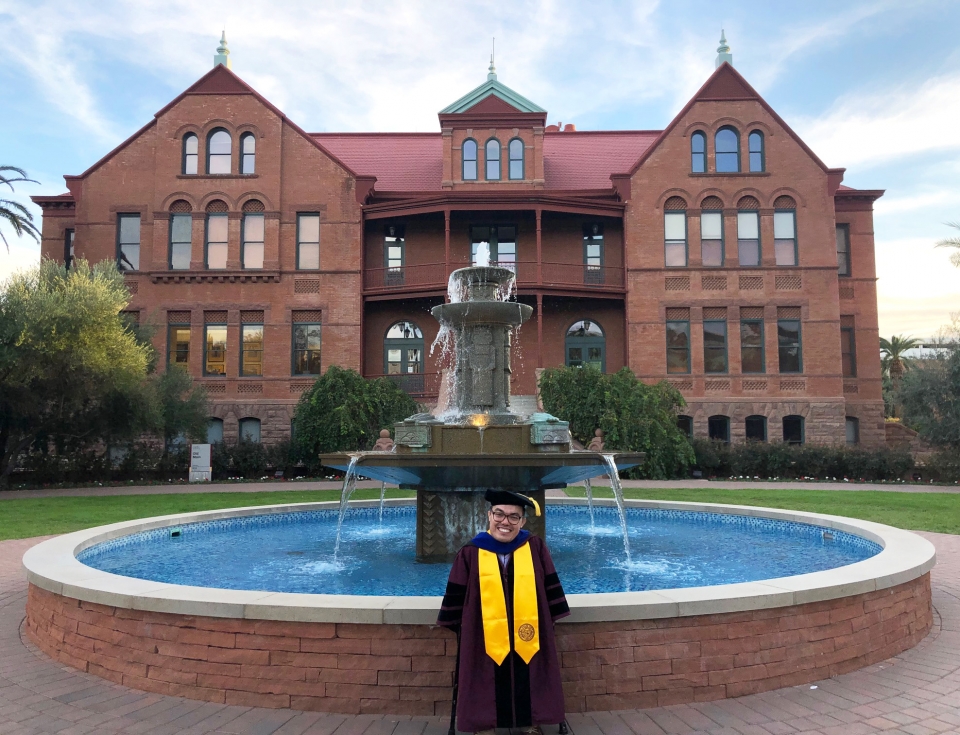 student standing in front of Old Main wearing graduation robes