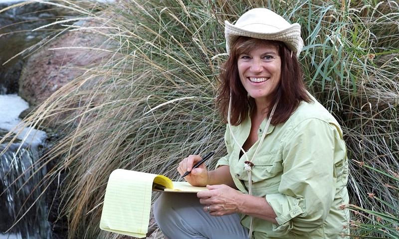 Nancy Grimm writes on a legal pad beside a desert stream