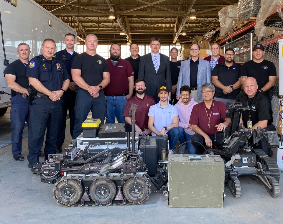 A group photo of Phoenix Police Department officers and ASU faculty, staff and students with two retired bomb squad robots. 