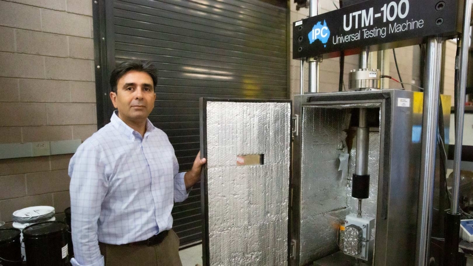 Photograph of Hasan Ozer in front of a pavement testing chamber