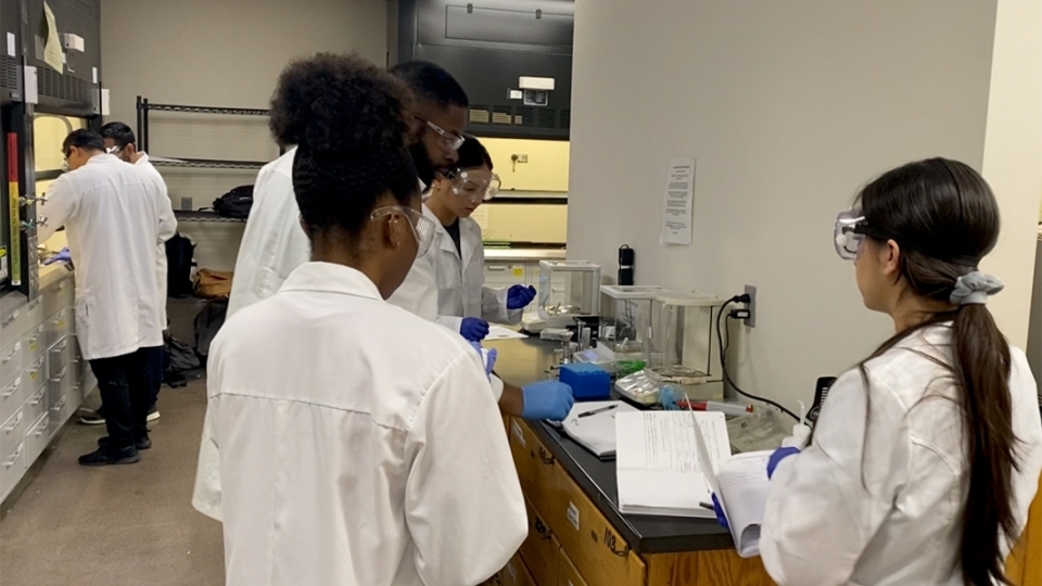 ASU Online students wearing white lab coats, gloves and goggles in a lab.