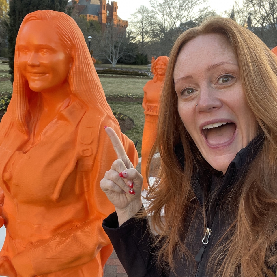 woman pointing at orange statue of herself