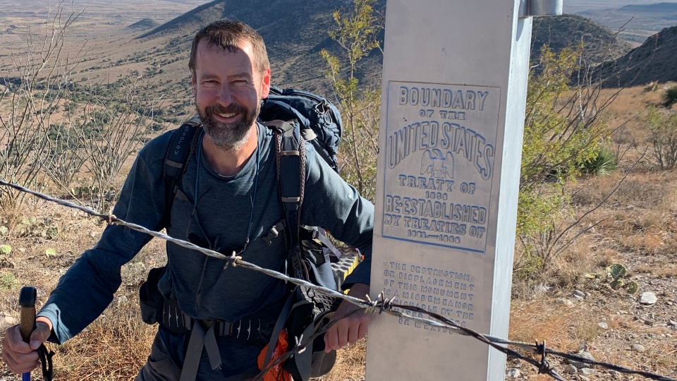 Man hiking, standing next to boundary marker