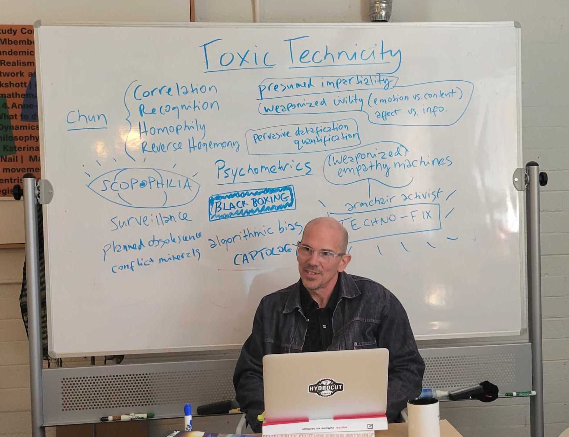Professor Marcel O'Gorman sitting in front of a whiteboard with a brainstorm written on it.
