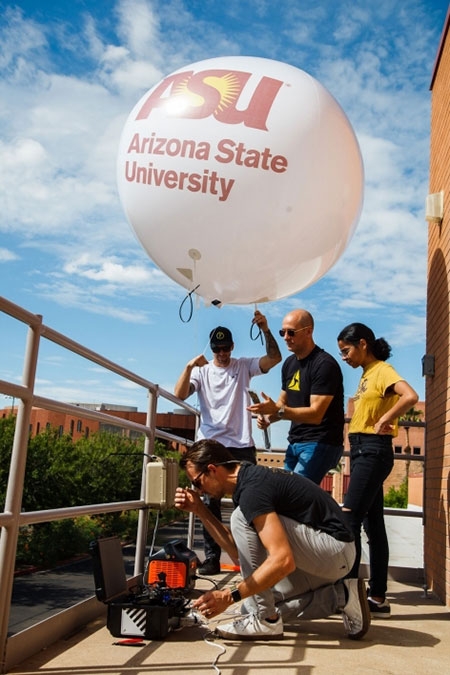 A group of four from ASU and Axon work on camera equipment and balloons on the roof of the Memorial Union building on ASU's Tempe campus.